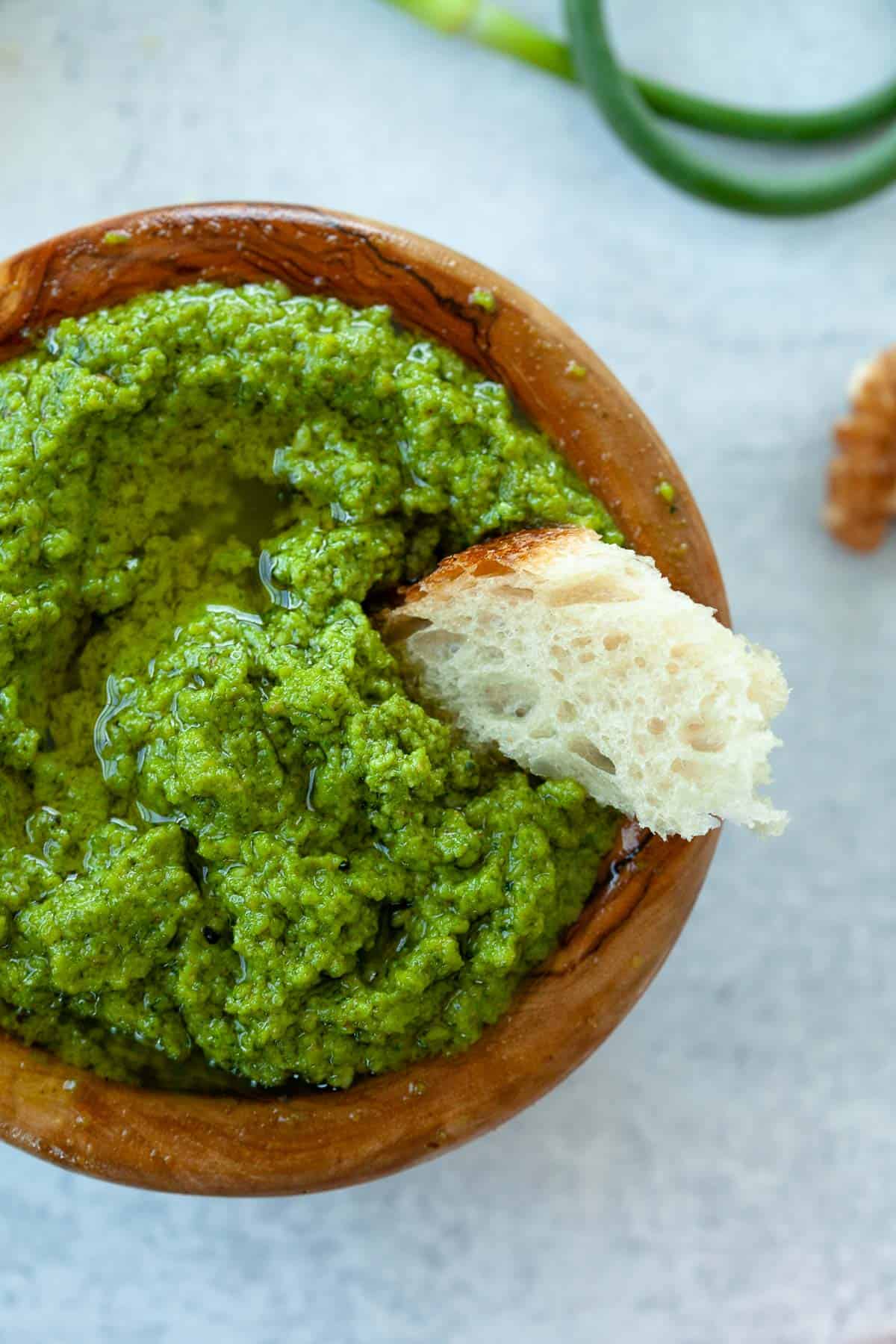 pesto in small wooden bowl. piece of baguette dipped in. 