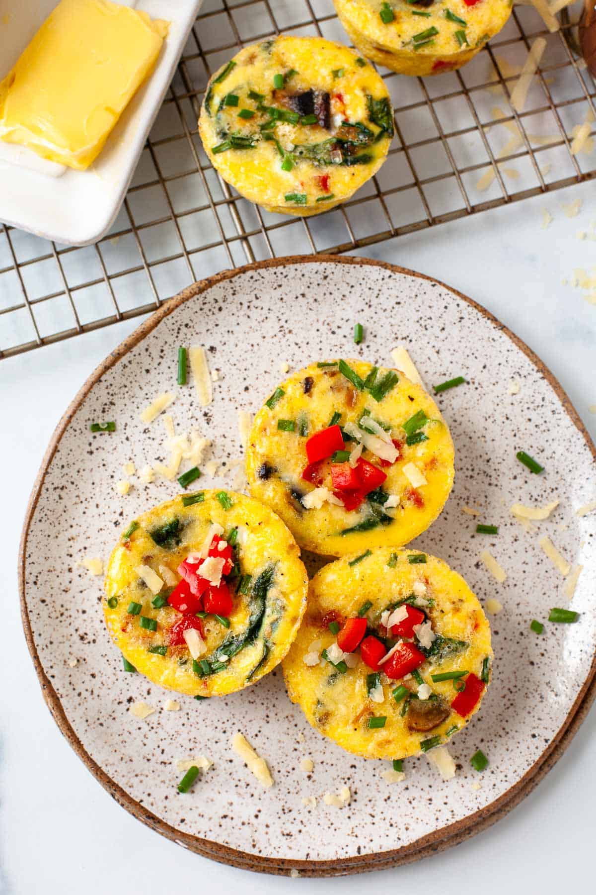 3 egg bites on speckled plate. wire rack. slab of butter. egg bite on wire rack.