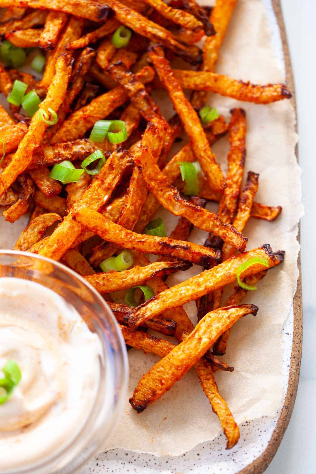 crispy kohlrabi fries close up. pieces of sliced scallion. glass bowl of dip blurred in background.