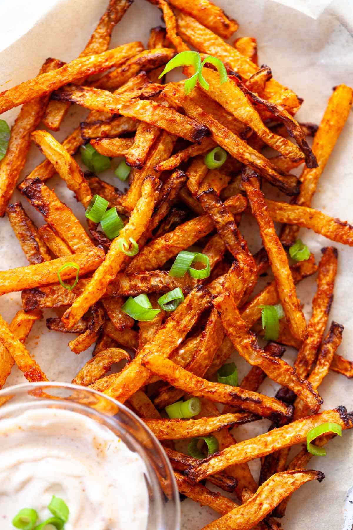 crispy kohlrabi fries. scallion garnish. on parchment paper. dip on the side.