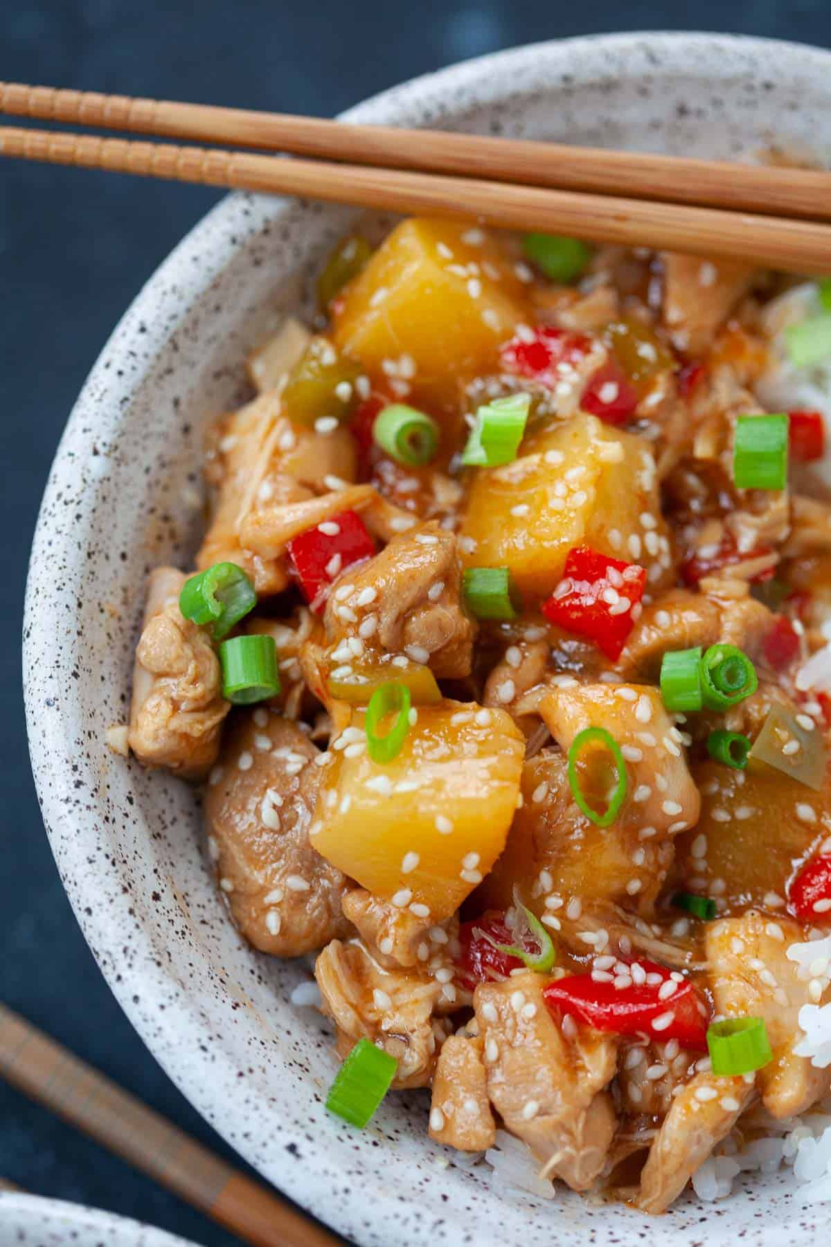 sweet and sour chicken served in grey speckled bowl with white rice and chopsticks