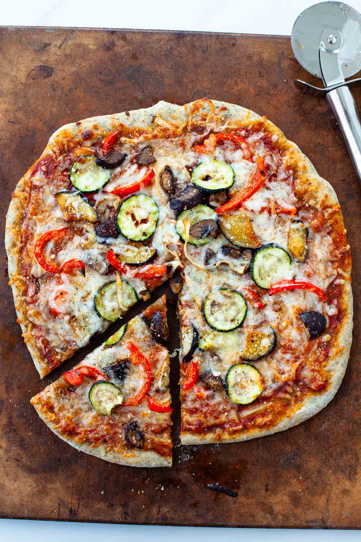 roasted vegetable pizza on pizza stone with pizza cutter and slice cut out