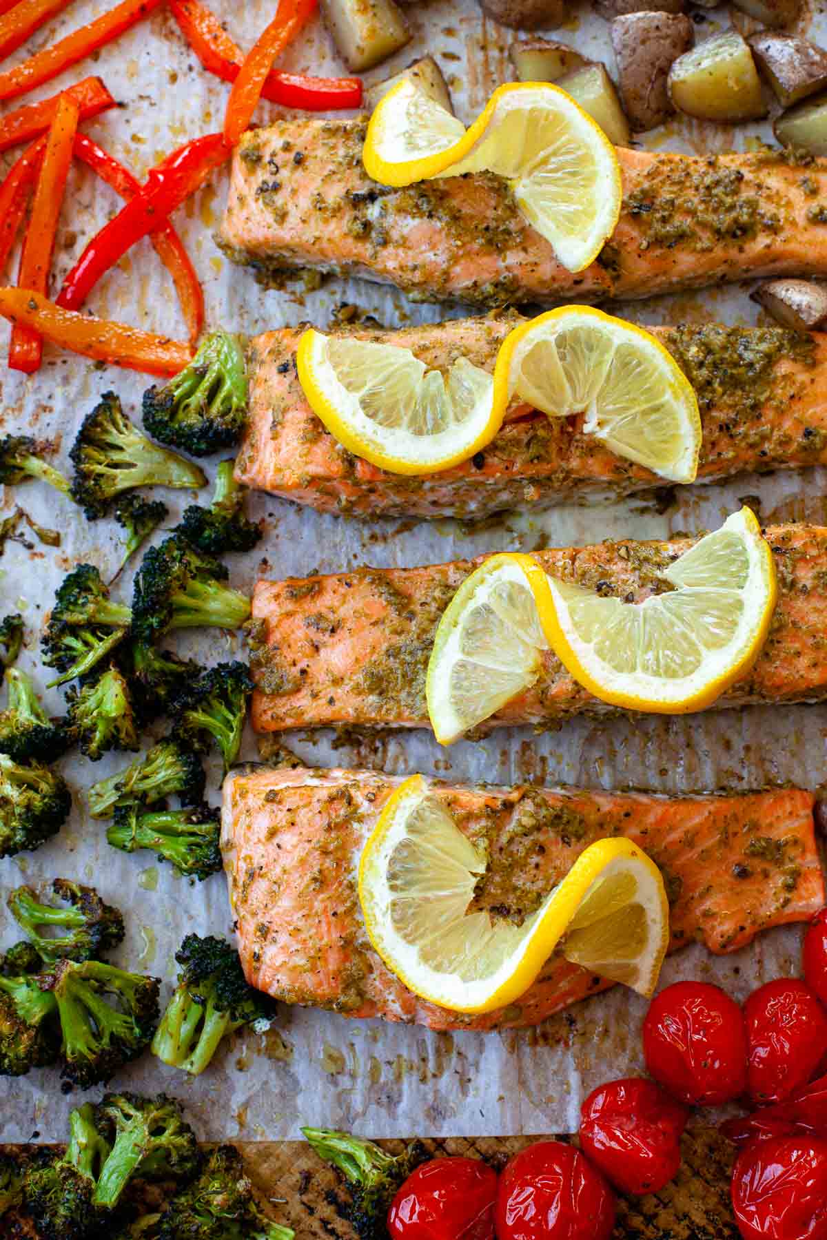 sheet pan salmon with pesto salmon with lemon slices, broccoli, red bell pepper, potatoes, tomatoes