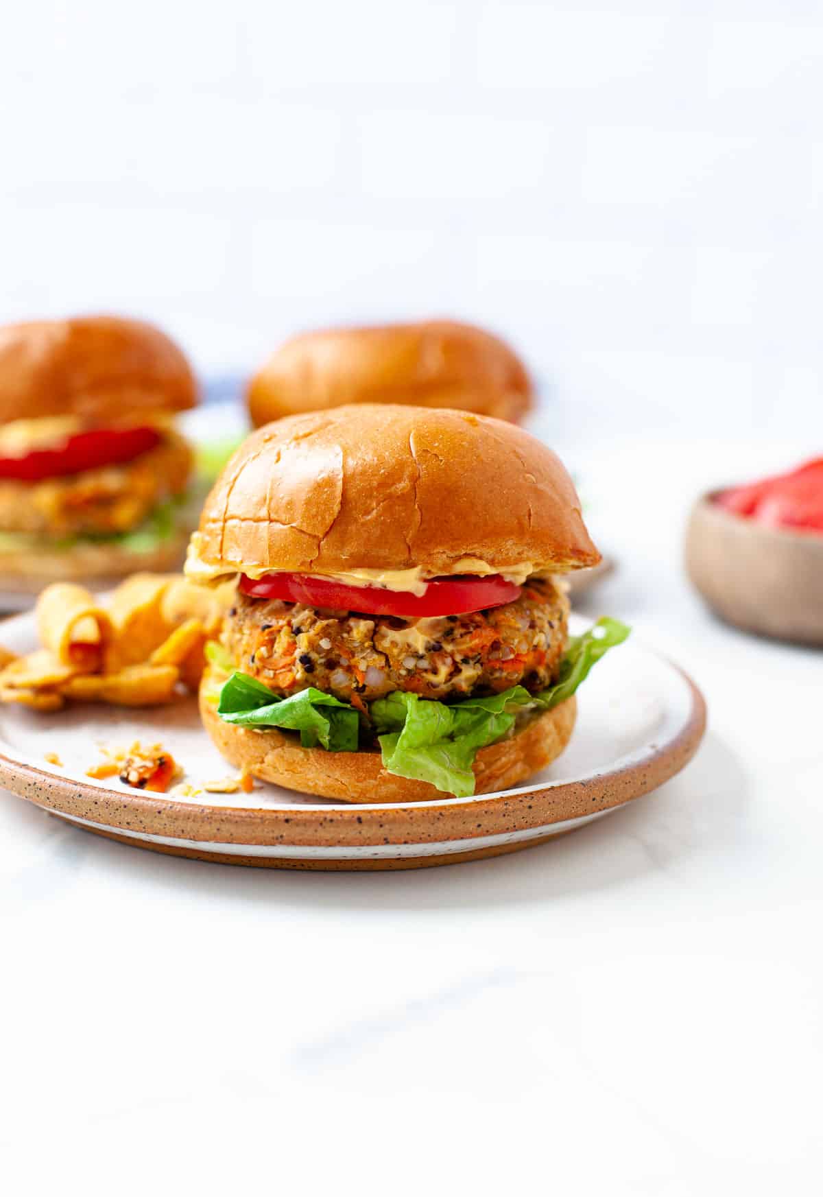 three vegan chickpea burgers with lettuce, tomato, vegan aioli on white and brown plate
