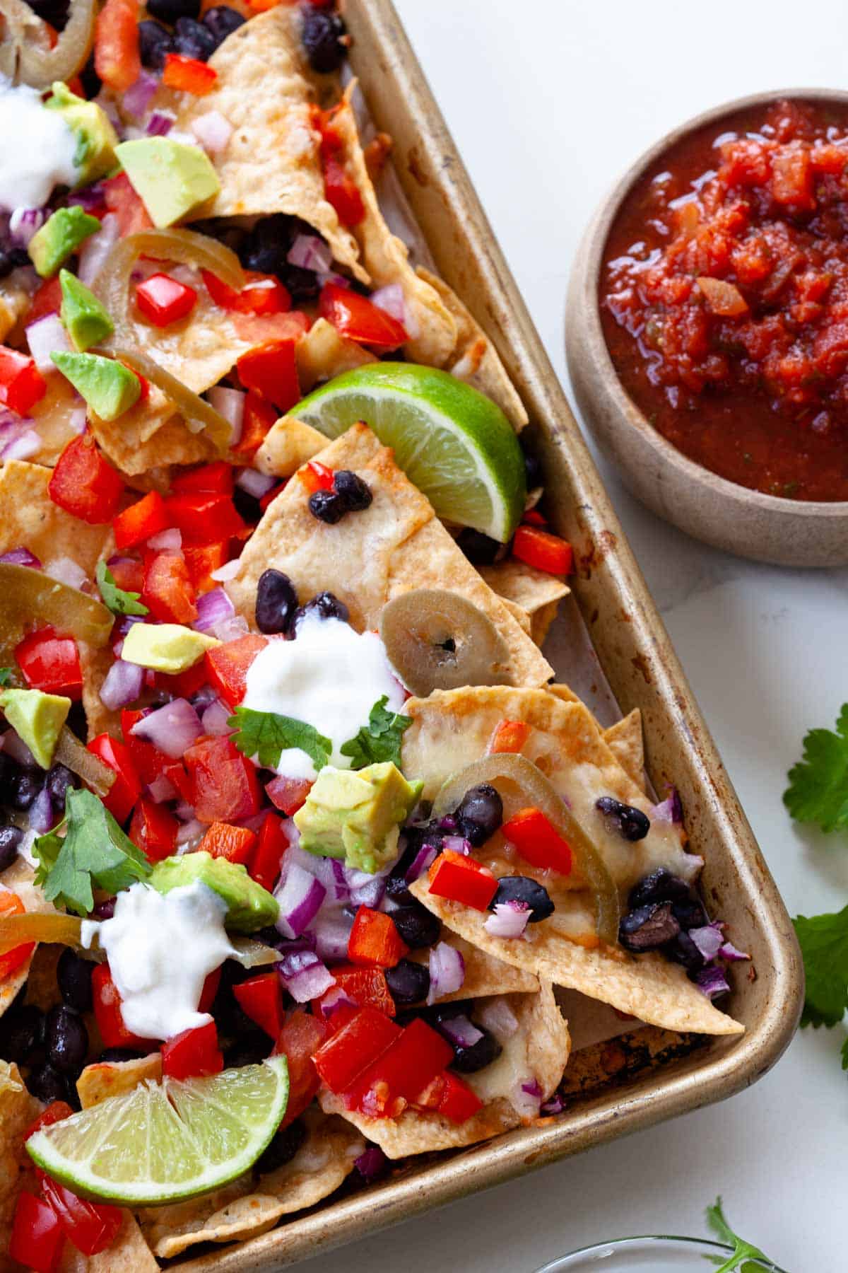 close up vegetarian nachos with toppings like avocado, limes, cilantro and bowl of salsa on the side