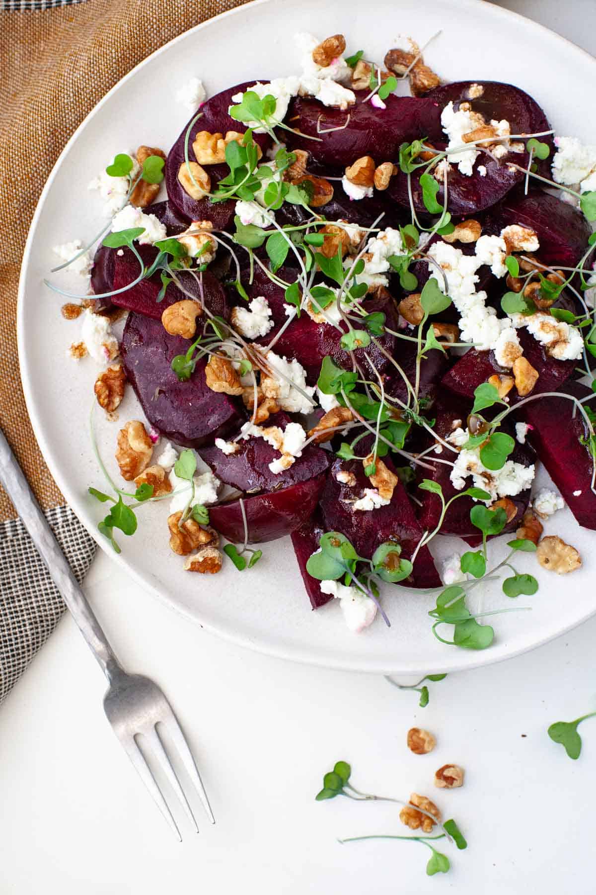 Beetroot salad with feta on white dish alongside kitchen towel and small silver fork