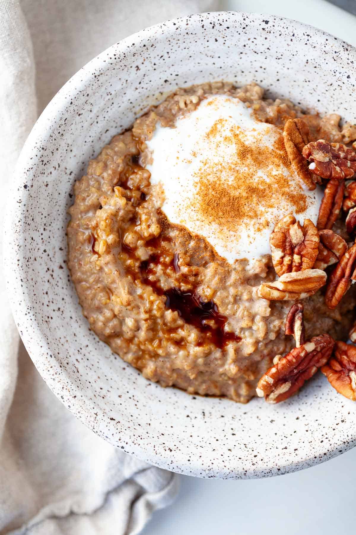Gingerbread Oatmeal in white speckled bowl topped with yogurt, pecans, molasses, and cinnamon.